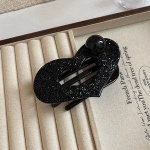 Macro view of a black hollow heart hair claw clip with rhinestones on a jewelry tray