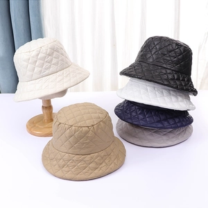 Close-up of quilted diamond pattern winter bucket hats in multiple colors on a wooden stand