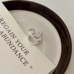 Minimalist silver irregular hollow ring displayed on a ceramic plate with decor card