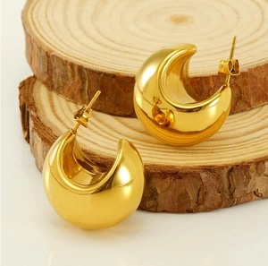 Close-up of golden teardrop hoop earrings placed on a natural round wooden base