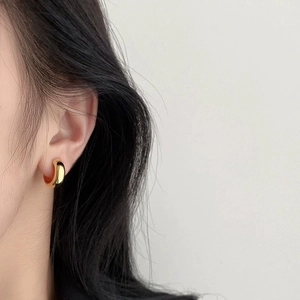 Close-up of a stylish gold geometric hoop earring worn on the earlobe with a matte finish