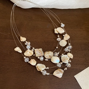 Detail of layered necklace with natural shell fragments and crystal beads on wood