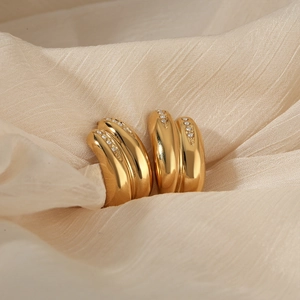 Gold stainless steel double hoop earrings with zirconia stones on a beige fabric background