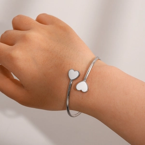 Detail of silver open cuff bracelet featuring white enamel double heart charms on wrist