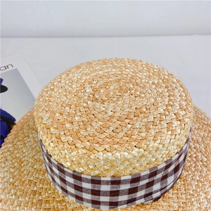 Détail du haut d'un chapeau de paille avec tissage fin et ruban décoratif à carreaux bruns