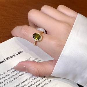 Detail of an 18k gold plated ring featuring an oval green gemstone and diamond accents
