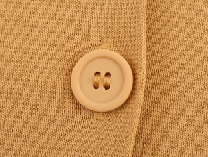 Macro shot of circular button and tight camel knit fabric texture on the cardigan