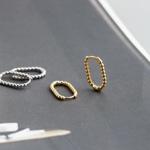 Detailed view of U-shaped gold and silver beaded hoop earrings on a dark textured surface