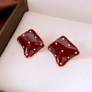 Deep red square earrings with white dots and gold edges on a minimalist jewelry box