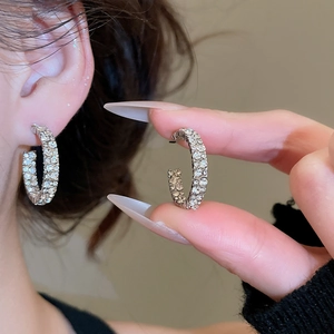 Detailed close-up of C-shaped silver earrings with sparkling zircon pave setting