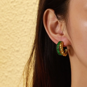 Detail of vintage C-shape twisted gold earrings with rectangular green gemstones on model