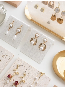 Macro shot of vintage pearl and metal earrings on a textured acrylic jewelry display
