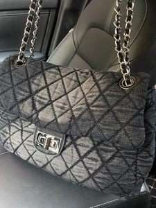 Detail of black denim quilted bag featuring silver chain strap and metal turn-lock closure