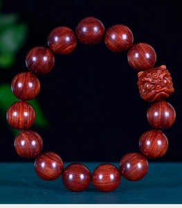 Macro view of polished dark red wood beads and intricate mythical beast carving on the bracelet