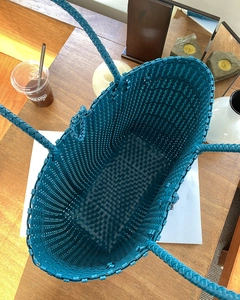Draufsicht auf große türkisfarbene geflochtene Tragetasche auf einem Holztisch mit Deko