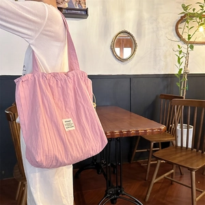 Detailed texture of pink pleated knit tote bag worn in a cozy cafe setting