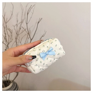Handheld view of a quilted floral cotton mini cosmetic bag with a blue ribbon bow detail