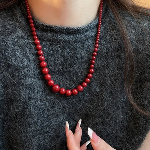 Gros plan d'un collier de perles rouges dégradées sur un pull gris au drapé élégant