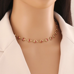 Detail of gold heart link necklace with red stones worn on model with beige blazer
