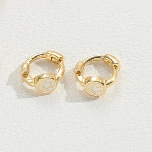 Macro view of gold hoop earrings featuring white smiley face charms on white background