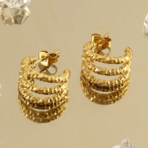 Close-up of golden multi-layered hoop earrings with hammered texture on a mirror
