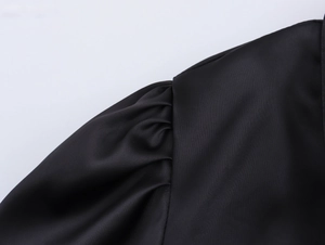 Detailed view of puff shoulder design and ruched satin fabric on black V-neck dress