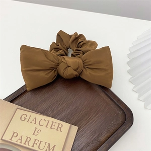 Detail view of a brown satin bow scrunchie placed on a wooden tray with minimal props