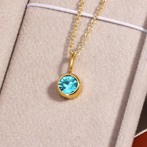 Close-up of the round blue birthstone pendant set in a polished golden necklace chain