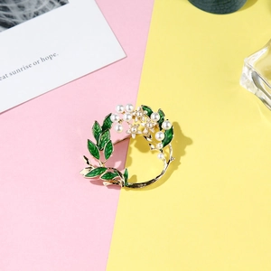 Macro shot of wreath brooch with green enamel leaves and white pearls on gold base