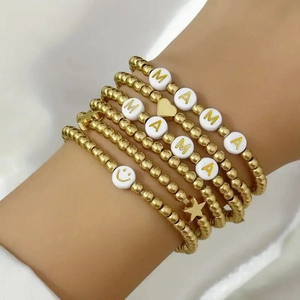 Detail of layered gold beaded bracelets featuring MAMA letter charms and heart accents