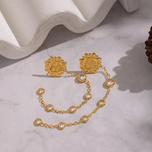 Detail of sun-shaped gold tassel earrings with zircon stones on marble background