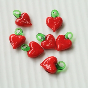 Macro shot of red heart-shaped glass fruit pendants with green loops for DIY jewelry making