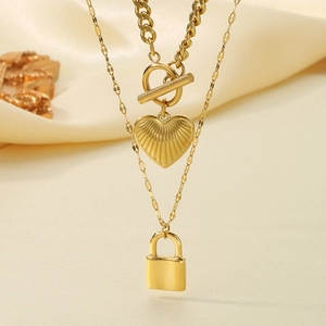 Detail of gold double-layered necklace with heart and lock pendants on beige silk
