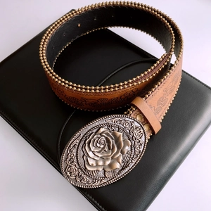 Close-up of vintage bronze rose relief buckle on brown leather belt with metal bead trim