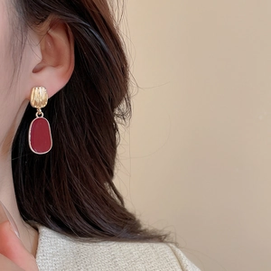 Detail of model wearing gold tone earrings with dark red oval pendants and metal discs