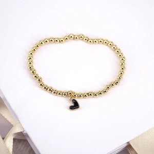 Golden beaded bracelet with a black enamel heart charm on a white gift box
