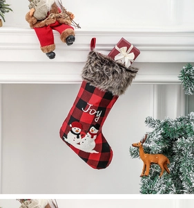 Détail de chaussette de Noël à carreaux rouges avec broderie Joy sur cheminée blanche