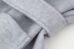 Détail d'un manteau en laine gris montrant la texture du tissu et les coutures de qualité