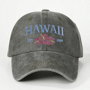 Dettaglio ravvicinato del ricamo blu HAWAII e dei fiori di ibisco sul berretto grigio lavato