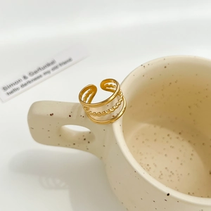 Three-layer gold open ring displayed on a beige ceramic mug with artistic splatter