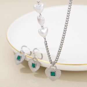 Detail of silver necklace and earrings set with green stones and heart pearls on a plate