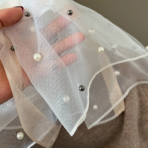 Detail of sheer white mesh scarf featuring elegant white and grey pearl embellishments