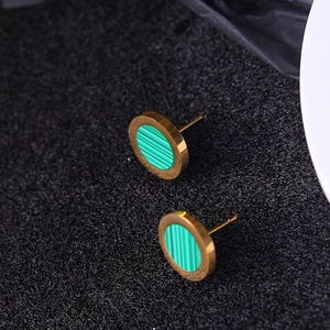 Macro shot of gold-plated circular stud earrings with green stripe inlay on black fabric