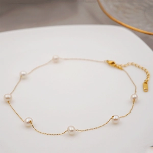 Elegant gold titanium steel necklace featuring dainty white freshwater pearls on a white plate