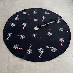 Detail of black knitted Christmas tree skirt with red candy cane and white snowflake patterns