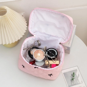 Macro shot of pink quilted makeup bag with bow embroidery and cosmetics inside