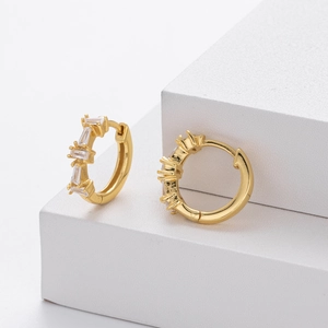 Detailed view of gold earrings with rectangular white zircons on a white geometric block