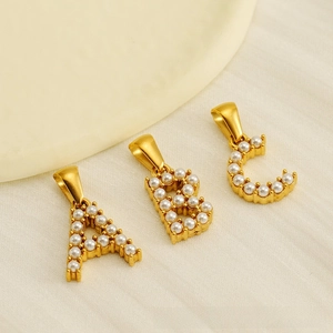 Détail macro de pendentifs lettres A, B, C dorés sertis de petites perles blanches