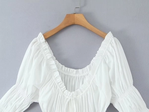 Détail des manches bouffantes et de l'encolure froncée sur une chemise longue blanche