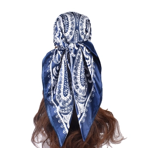 Detail of silk satin headscarf with navy paisley print tied on model long curly hair